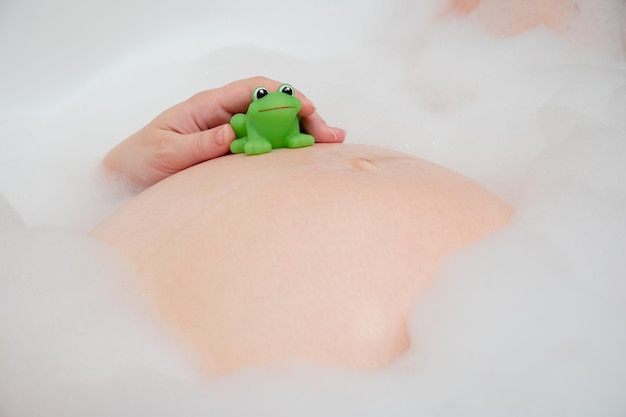 Pregnancy belly with green frog toy closeup Pregnant woman having bubble bath