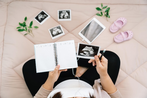 A Pregnancy dairyTop view of pregnant woman writing thoughts down in notebook for memoryxray image of her baby and shoesConcept of pregnancy Maternity prenatal care