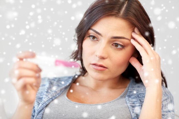 pregnancy, fertility, infertility, maternity and people concept - sad unhappy woman looking at pregnancy test at home over snow