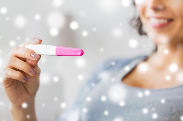 pregnancy, fertility, maternity and people concept - close up of happy smiling woman with home pregnancy test over snow