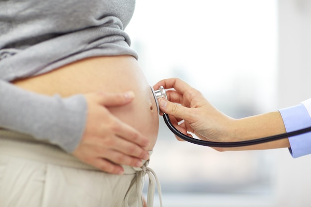 pregnancy, healthcare, people and medicine concept - close up of pregnant woman belly and doctor hand with stethoscope at medical appointment in hospital