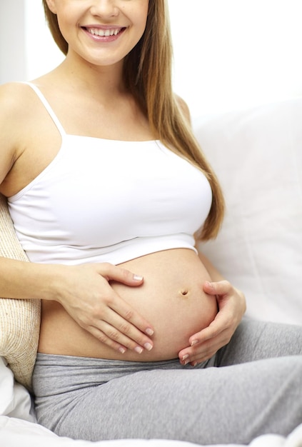 pregnancy, motherhood, people and expectation concept - close up of happy pregnant woman with bare tummy at home