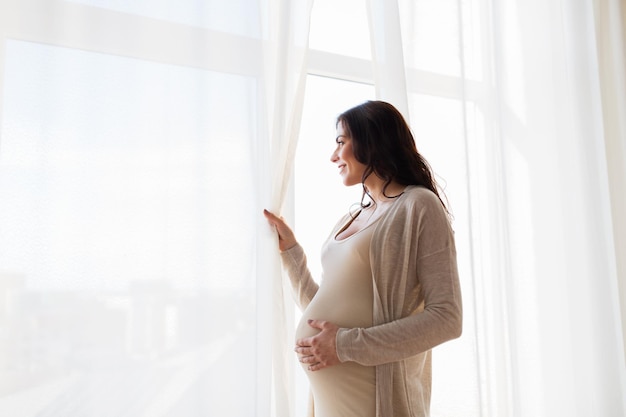 pregnancy, motherhood, people and expectation concept - close up of happy pregnant woman with big belly looking to window