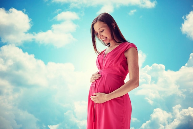 pregnancy, motherhood, people and expectation concept - happy pregnant woman with big tummy over blue sky and clouds background