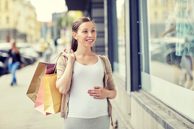 pregnancy, motherhood, people and expectation concept - happy smiling pregnant woman with shopping bags at city street