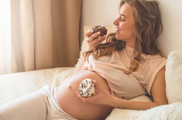 Pregnancy and nutrition. Pregnant woman enjoying donuts and tea in bed, free space