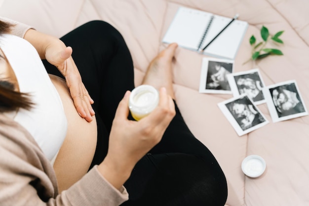 A pregnancy people and maternity concept  close up of pregnant woman applying stretch mark cream to belly