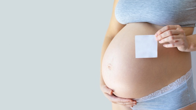 Pregnancy promo. white sheet in hand of pregnant woman on gray background.