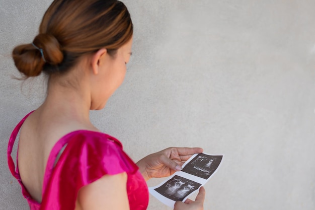 A pregnancy women is look at scan baby image with happy smile and cement wall background