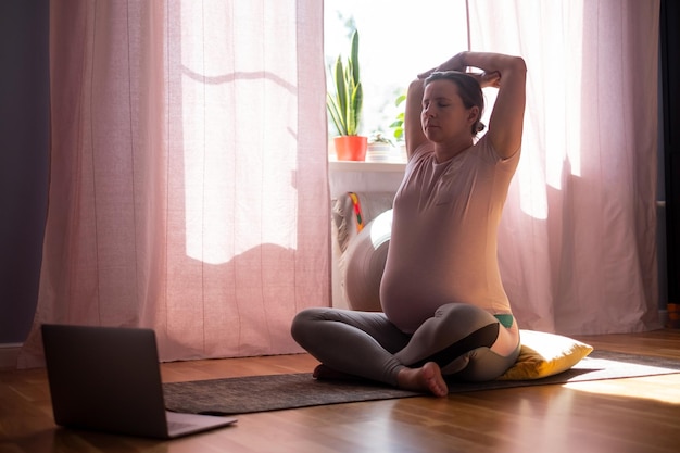 Pregnancy yoga meditation. Full length healthy pregnant woman doing yoga exercise at home. Hand stretch positions.