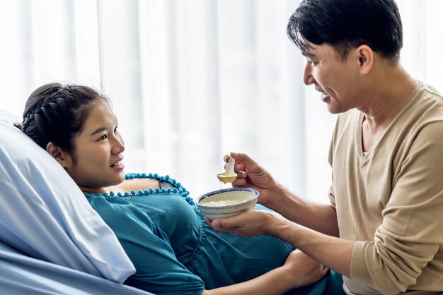 A pregnant Asian woman lay in a patient' bed and Her husband takes care By feeding a soft food