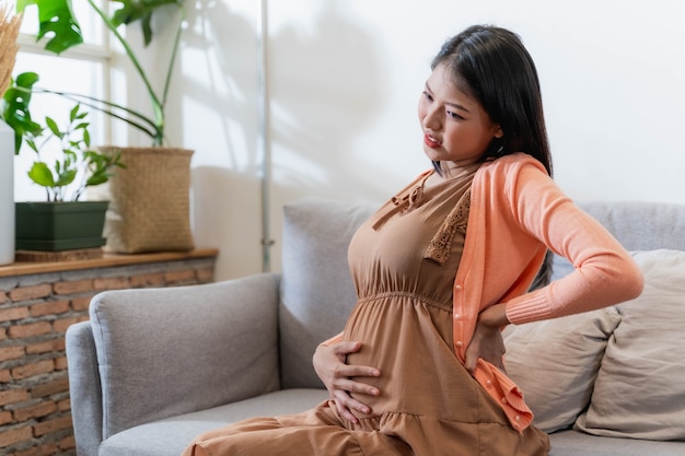 Pregnant asian woman suffering from back pain. beautiful pregnant woman touching her tummy and keeping one hand on her back