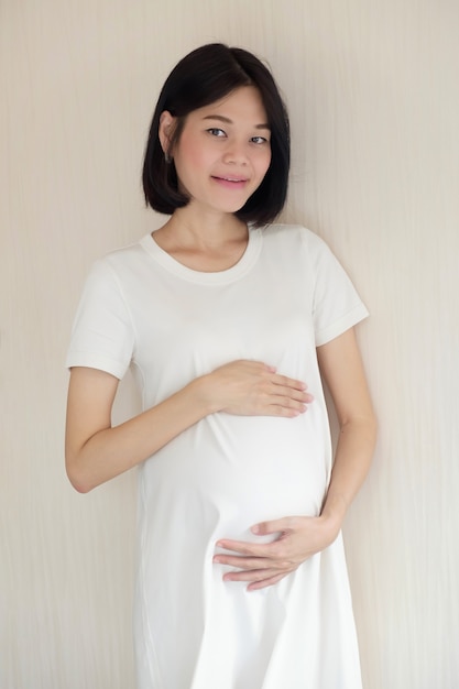 A pregnant Asian woman wearing casual clothes is standing at bed room.