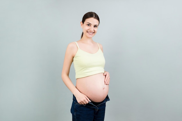 pregnant belly at colorful background with copy space Future mother in opened jeans is embracing her naked baby bump Motherhood concept