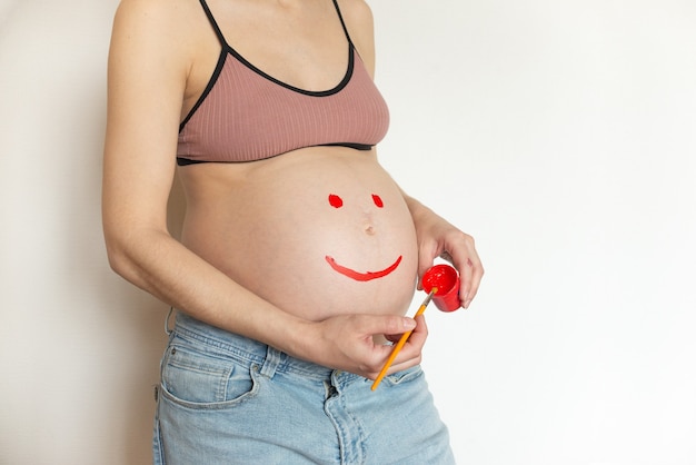 Pregnant belly girl with a smile drawn on her belly. Copyspace