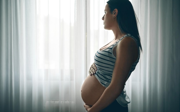 Pregnant caressing her nacked belly in front of a curtain