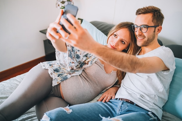 Pregnant couple lying on bed relaxing taking selfie