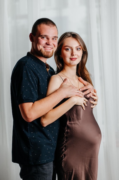 Photo a pregnant girl in a brown dress stands in an embrace with a man