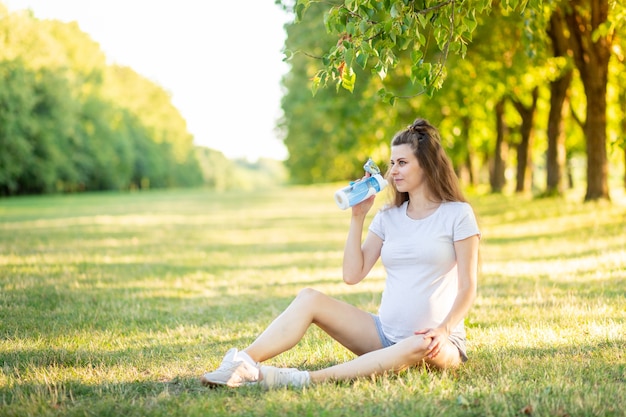 A pregnant girl does sports in nature in the summer, yoga for pregnant women in the fresh air