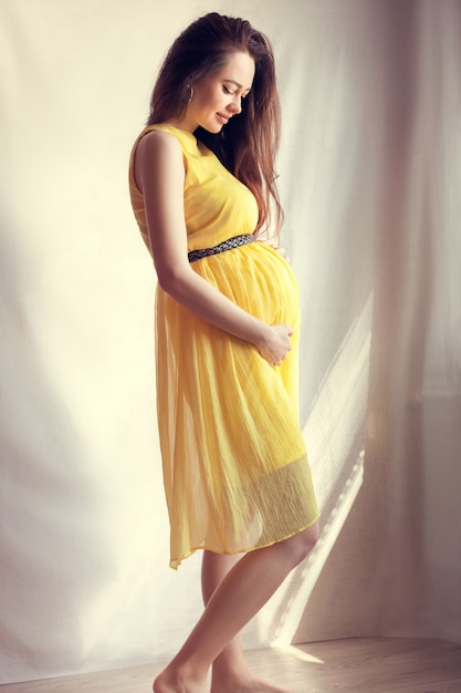 Pregnant girl dressed in yellow dress, holds herself tummy