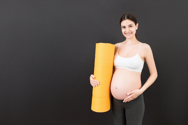 Pregnant Girl Holding Yoga Mat Standing Over Colored Background Studio Shot Free Space For Design