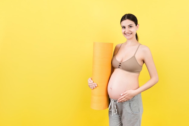 Pregnant Girl Holding Yoga Mat Standing Over Colored Background Studio Shot Free Space For Design