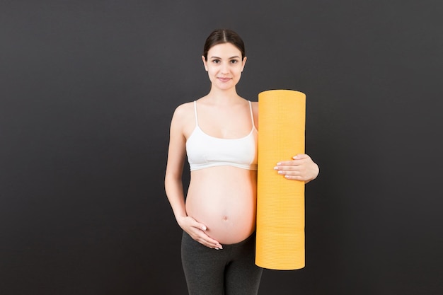 Pregnant Girl Holding Yoga Mat Standing Over Colored Background Studio Shot Free Space For Design