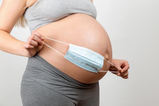 A pregnant girl holds a medical mask near her abdomen a symbol of protection against the coronavirus