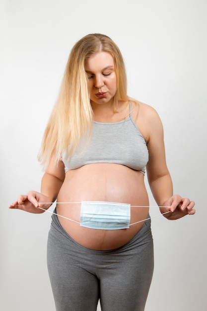 A pregnant girl holds a medical mask near her abdomen a symbol of protection against the coronavirus