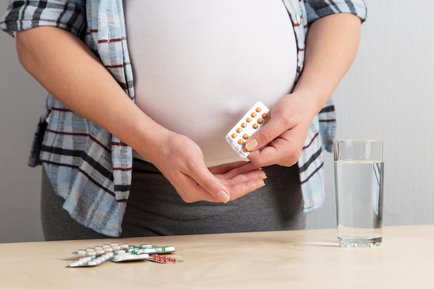 A pregnant girl holds pills and a glass of water Concept taking a large number of medications during pregnancy