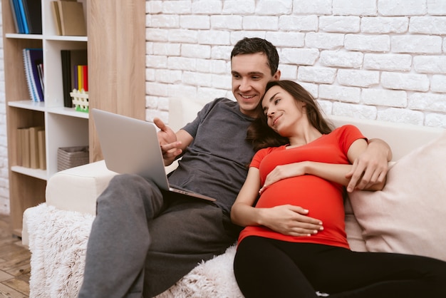 Pregnant girl is sitting with a man and watching something.