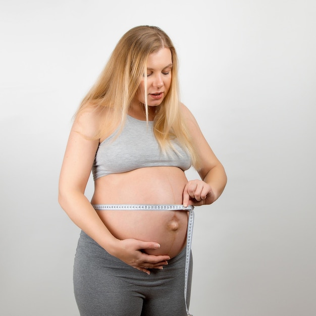 A pregnant girl measures her stomach with a tapeline Tracking the growth progress of the abdomen and baby