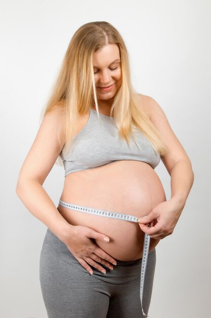 A pregnant girl measures her stomach with a tapeline Tracking the growth progress of the abdomen and baby