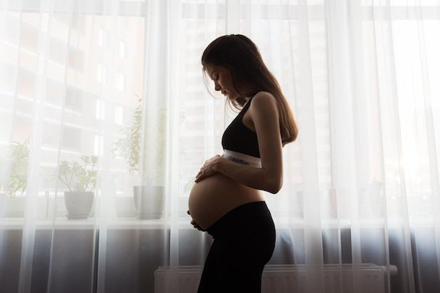 Pregnant girl in pajamas standing by the window