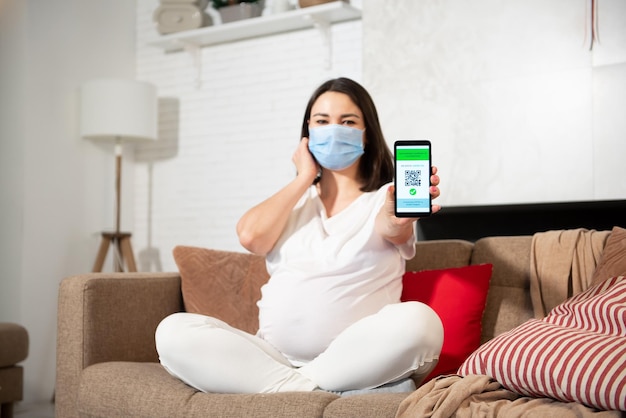 A pregnant girl in a protective face mask shows a vaccination certificate on her phone