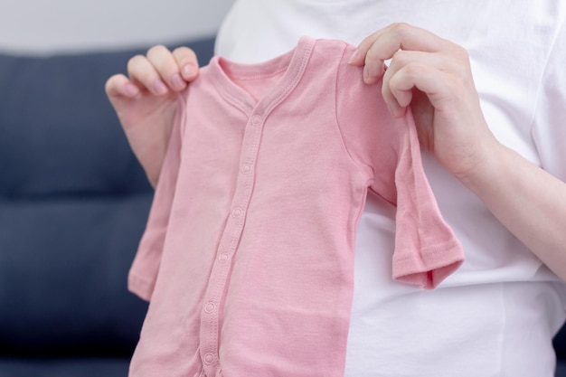 A pregnant girl sits on a sofa and puts baby clothes on her stomach