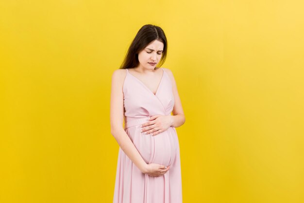 A pregnant girl who has a stomach ache stands on a colored background isolated