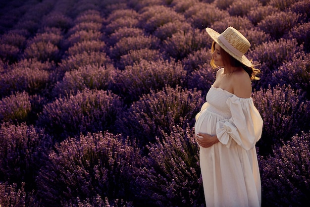 The pregnant girl with a hat in the lavender field on a sunset