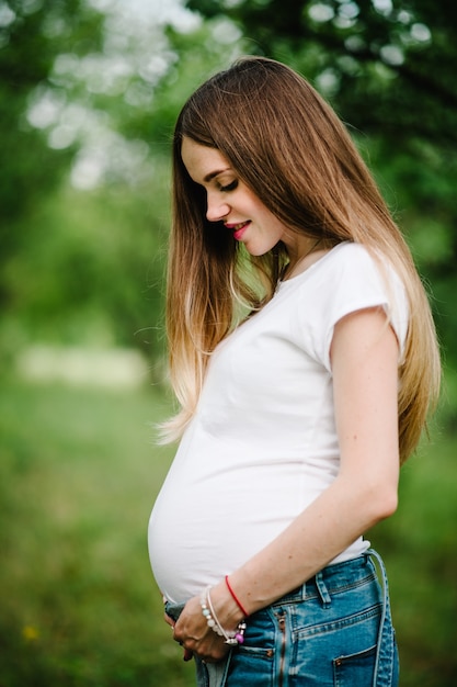 Pregnant happy girl stands and holds hands on stomach. Close up. upper half. Looking down