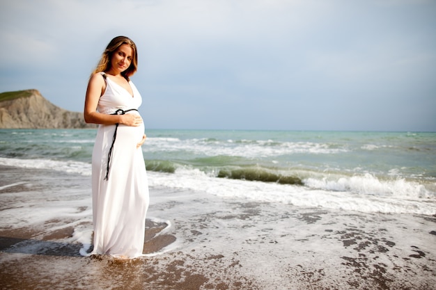 Pregnant lady standing on beach near sea