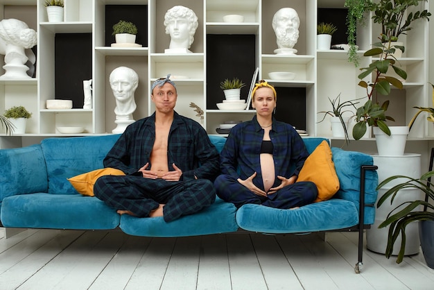 A pregnant man and woman are meditating in a lotus position on the couch