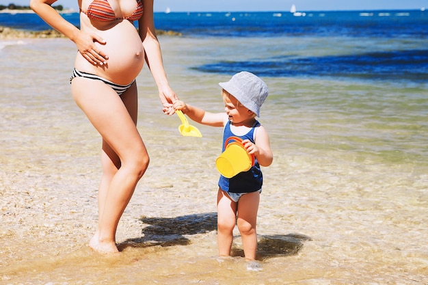 Pregnant mother and her son little cute toddler child playing and relaxing on the sea beach