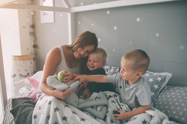 Pregnant mother and two sons are reading an interesting book at home in the morning. Casual lifestyle in bedroom