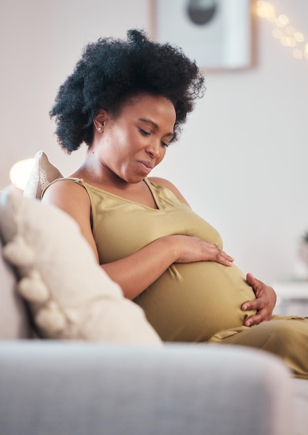 Pregnant sofa and black woman hands with hope feeling relax and mother love Mom care couch and living room lounge with a person holding abdomen happy about pregnancy lifestyle and baby in a house