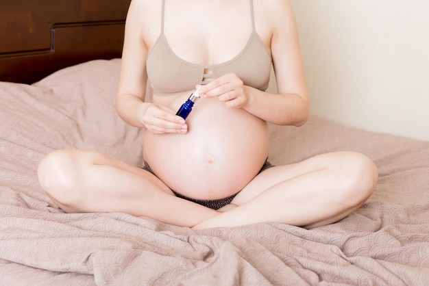 Pregnant woman applying stretch mark cream to belly pregnancy people and maternity concept pregnant apply antistretch mark cream on her belly