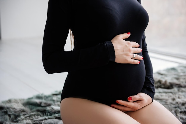 Pregnant woman in black bodysuit holding her belly