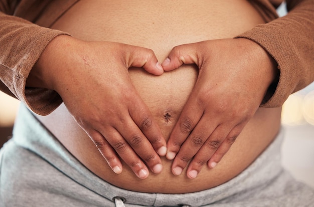 Pregnant woman closeup of heart hands on belly and happy black mother alone in Jamaica living room Excited future parent holding healthy abdomen at home and loving mommy in pregnancy care