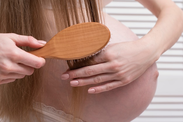 Pregnant woman combing her long hair. Close-up. Health concept