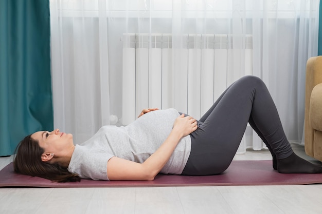 Pregnant woman does pilates on purple sports mat at home