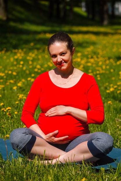 Pregnant woman doing asana sukhasana outdoors